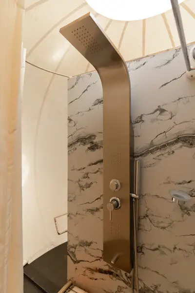 A modern brushed metal shower panel mounted on a white marble-veined wall inside a glamping dome. boche 1000 acre wayanad